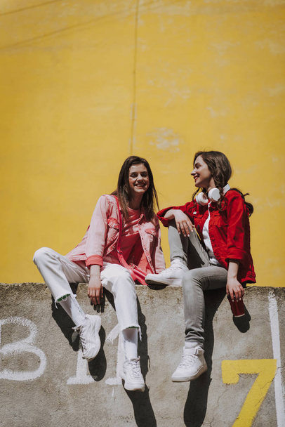 Two hipster girls sitting together on parapet - Foto, afbeelding