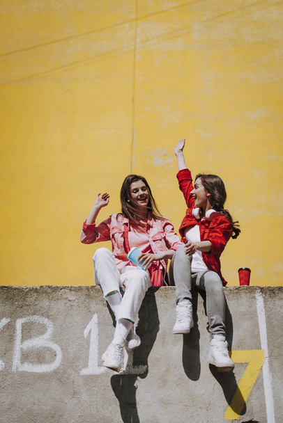 Two happy hipster girls sitting on parapet - Foto, Imagen