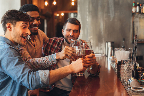 Male Friends Drinking Beer And Talking In Bar - 写真・画像