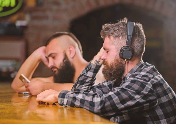 Friday relaxation in bar. Hipster bearded man spend leisure at bar counter. Order drinks at bar counter. Men with headphones and smartphone relaxing at bar. Avoid communication. Escape reality - Foto, afbeelding