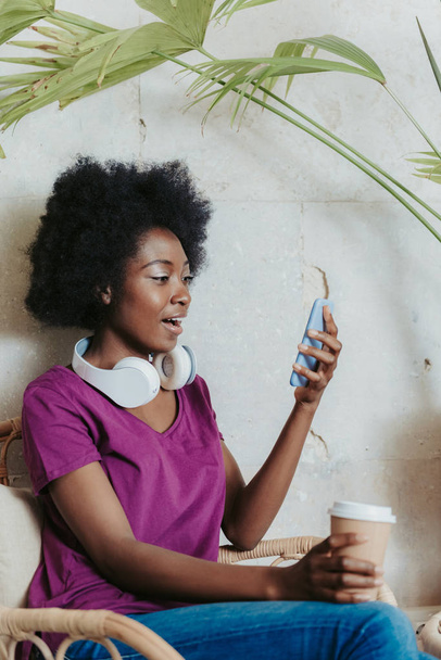Talia się wstrząśnięty African kobieta ubrany casual i patrząc na smartphone - Zdjęcie, obraz