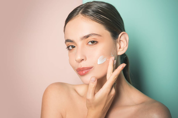 Beautiful woman spreading cream on her face. Skin cream concept. Facial care for female. Keep skin hydrated regularly moisturizing cream. Fresh healthy skin concept. Taking good care of her skin - Photo, Image