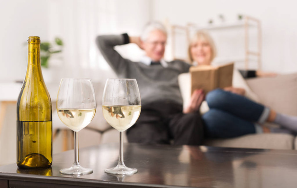 Γηραιότερος ζευγάρι ψάχνει άλμπουμ, πίνοντας κρασί στο σπίτι - Φωτογραφία, εικόνα