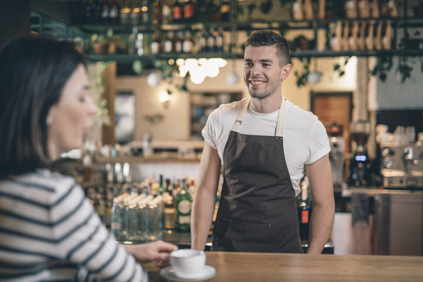 Cheerful barista standing at the bar counter and smiling - Photo, image