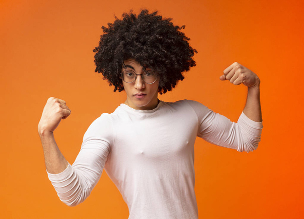 Félelmetes erős fekete fickó mutatja bicepsz narancssárga háttér - Fotó, kép