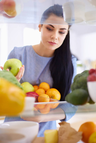 Smiling woman taking a fresh fruit out of the fridge, healthy food concept - Fotoğraf, Görsel