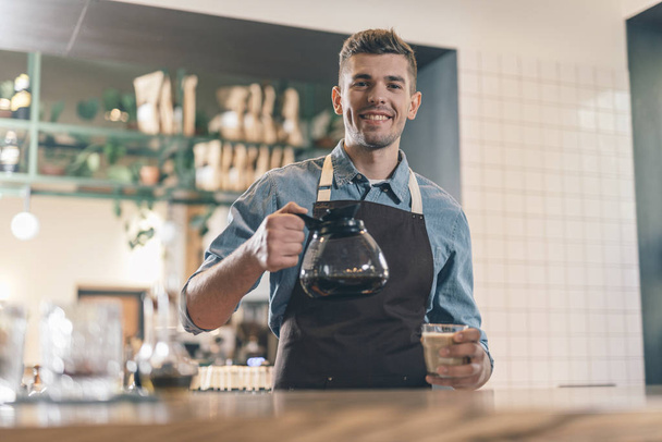 Friendly barista smiling at the camera while holding coffee - Foto, Imagen