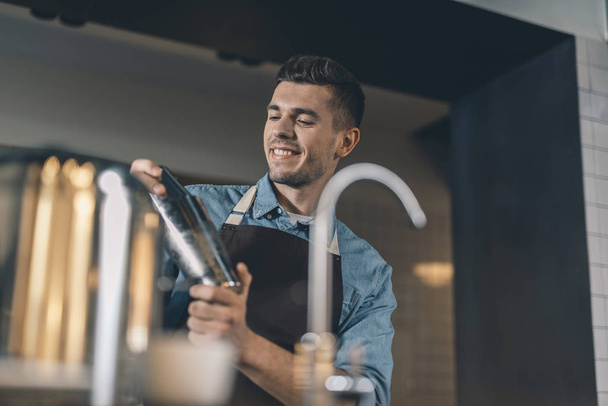 Happy young man making cocktails and smiling - 写真・画像