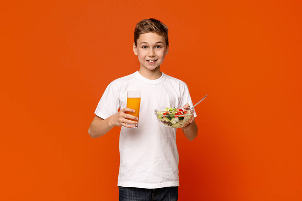 Smiling little boy eating vegetable salad and orange juice - Фото, изображение