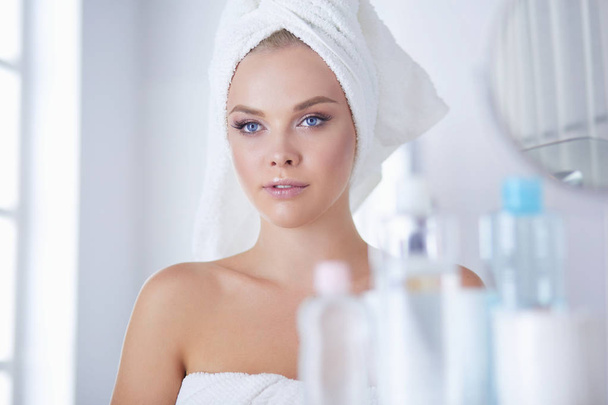Young woman in bathrobe looking in bathroom mirror - Foto, afbeelding