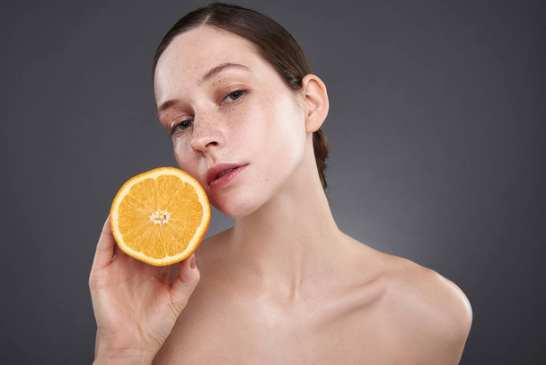 Attractive young woman with freckles holding orange half - Foto, Imagem