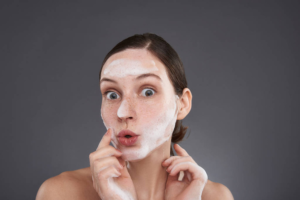 hübsches Mädchen mit Sommersprossen schmollen Lippen und waschen ihr Gesicht mit Seifenlauge - Foto, Bild
