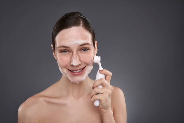 Charming girl using pore cleansing brush after bath - 写真・画像