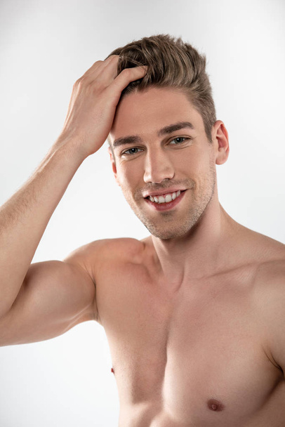Joyful handsome guy with perfect body touching his hair - Fotografie, Obrázek