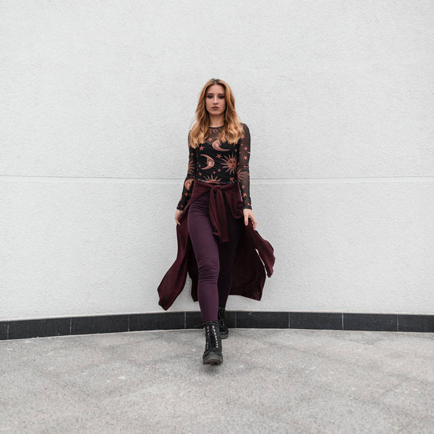 Urban red-haired young woman in a vintage black blouse in a pattern in pants in boots with a purple cape posing on the background of a white building. European girl model for a walk. Sreet style. - Fotografie, Obrázek