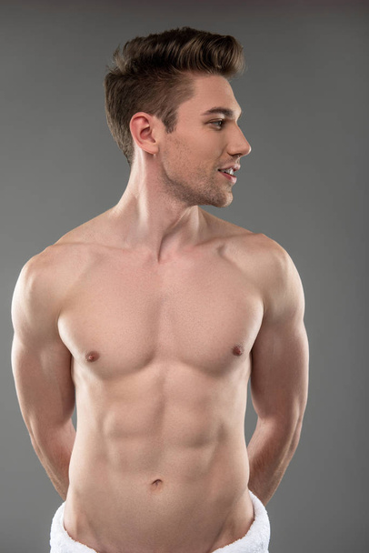 Handsome young man with perfect body standing against blue-gray background - Fotó, kép