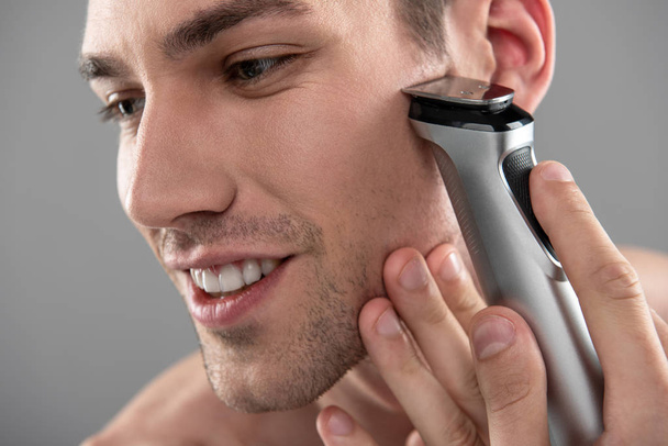 Joyful young man shaving with electric razor - Photo, Image