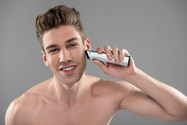 Smiling young man shaving with electric razor - Fotó, kép