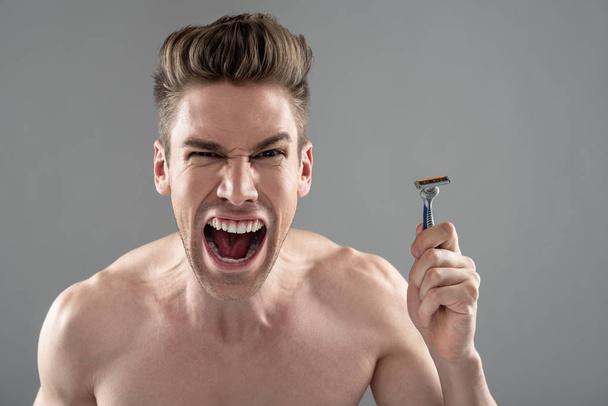 Angry young man holding disposable razor and screaming - Zdjęcie, obraz