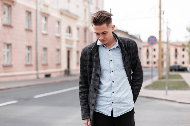 Urban stylish young guy with trendy hairstyle in fashionable elegant clothes  near vintage houses outdoors. Business guy travels through the city streets on a spring day. - Photo, Image