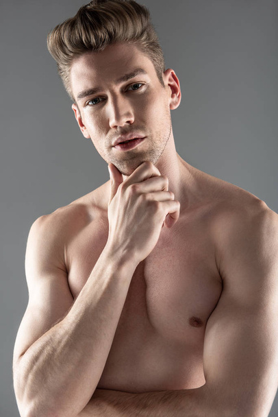 Attractive young man with muscular perfect body keeping hand on his chin - 写真・画像