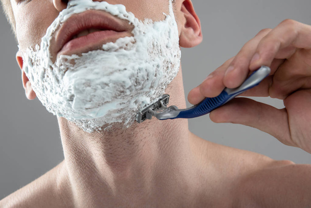 Young man shaving his stubble with disposable razor - 写真・画像