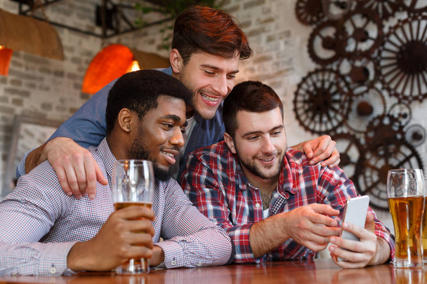 Onnelliset ystävät katsomassa videoita älypuhelimella ja juomalla olutta
 - Valokuva, kuva