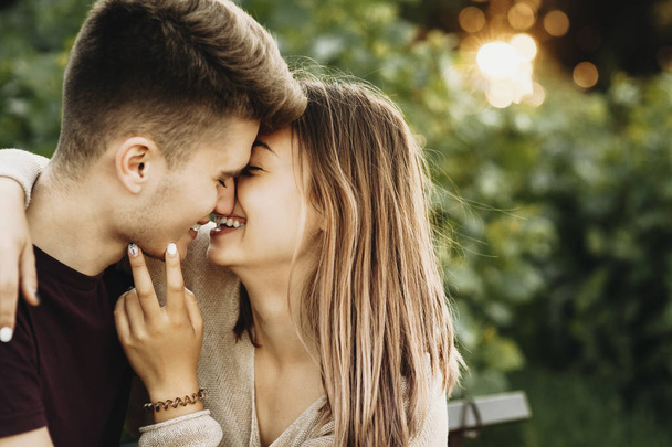 Retrato vista lateral de una encantadora pareja joven besándose y sonriendo contra el atardecer mientras citas en el parque
. - Foto, imagen