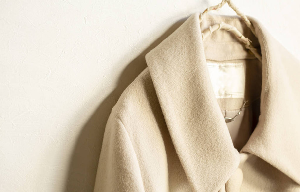 beige wool coat hanging on clothes hanger on white background - 写真・画像