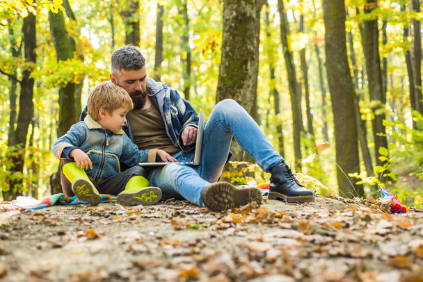 Schattige kleine jongen met zijn vader tijdens een wandeling in het bos. Vader speelt met een kleine zoon op een picknick in het Park in de vroege herfst dag. Ouder leren baby. - Foto, afbeelding