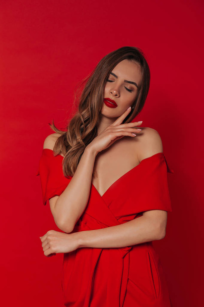 Studio portrait of attractive elegant woman with red lips wearing red dress posing on red background with closed eyes  - Photo, Image
