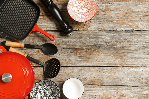 調理器具セット:木製テーブルの上に赤いエナメルキャスト鉄鍋、ソースパンとボウル、コピースペース付きのトップビュー - 写真・画像