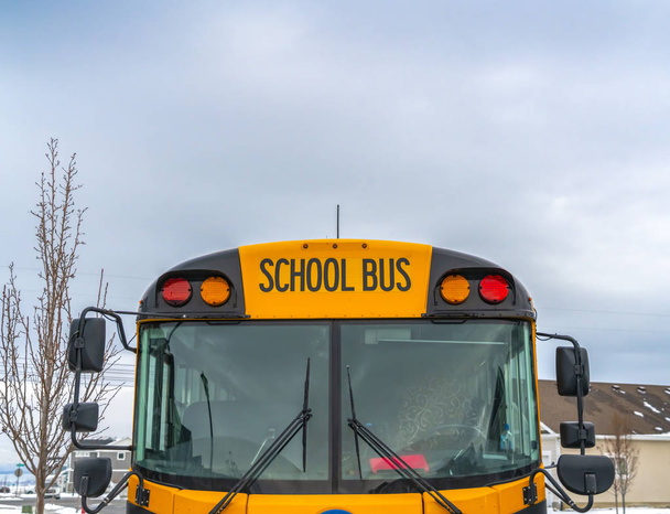 Вид спереду на жовтий шкільний автобус з будинками і хмарним небом на задньому плані
 - Фото, зображення