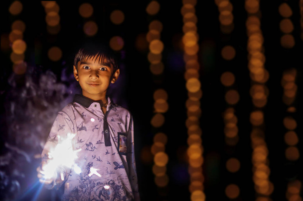 Cute Indian child celebrating Diwali festival with cracker and sparkle - Foto, Imagem