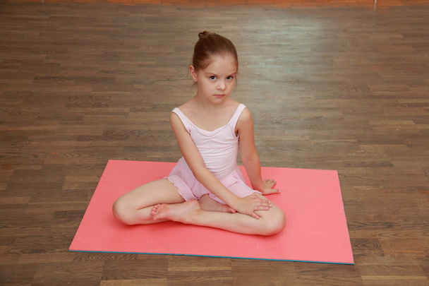 Lovely little girl doing sports exercises on the mat (stretching) - Фото, изображение