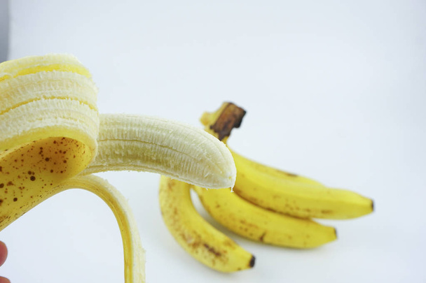 皮をむいたバナナを持つ手は白い背景を隔離した。健康的な栄養価の高い食品. - 写真・画像