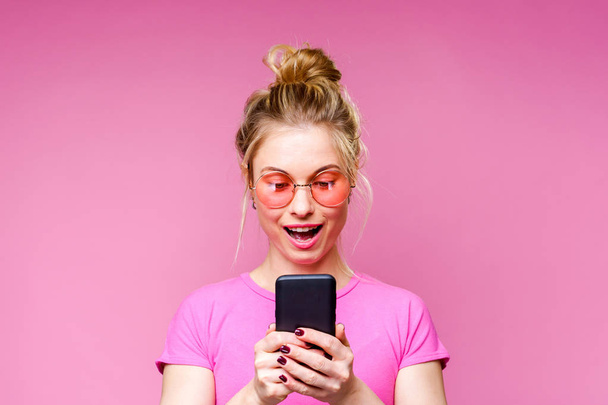 Photo of blonde in pink T-shirt with phone in her hands - Foto, Imagen