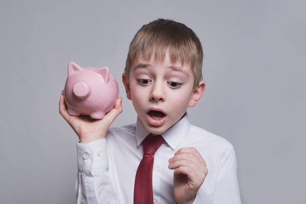 Boy listens attentively to the pink piggy bank. Business concept. Light background - Fotografie, Obrázek
