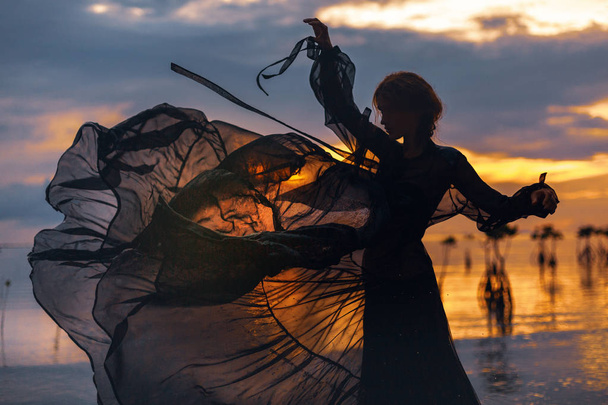 jovem mulher em pé na água ao pôr do sol silhueta
  - Foto, Imagem