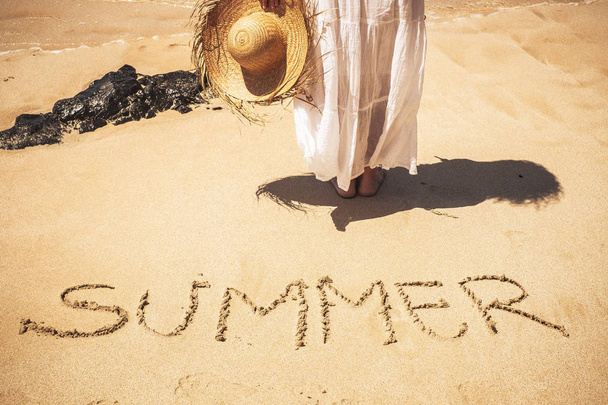 γυναίκα στην παραλία απολαμβάνοντας τον ήλιο με λέξη καλοκαίρι έγραψε στην άμμο  - Φωτογραφία, εικόνα
