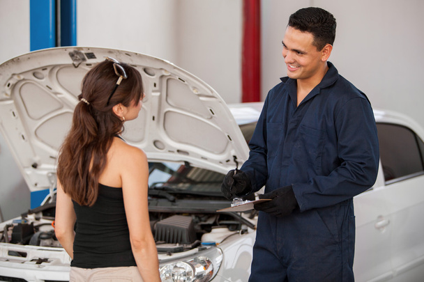 Mechanic standing next to a client in a garage - Fotó, kép