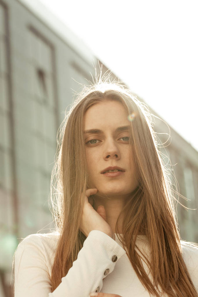 Retrato vertical de una joven con cabello rubio y ojos azules. Modelo posando en cámara en la calle
 - Foto, imagen
