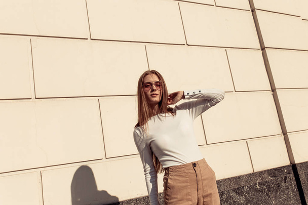 Girl posing against a white brick wall. Beautiful young woman wearing a white svidshot and wears sunglasses - Foto, Imagem