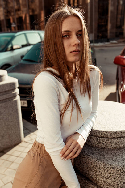 街の真ん中にカメラを向ける少女。スタイリッシュでファッショナブルな服に身を包んだ長いブロンドの髪を持つ美しいモデル. - 写真・画像