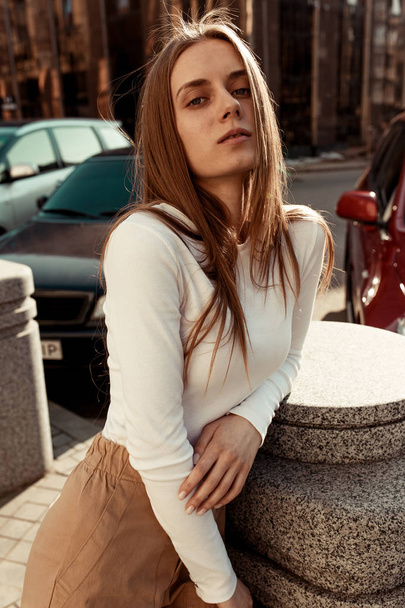 Nuori tyttö poseeraa kameran edessä keskellä kaupunkia. Kaunis malli pitkät vaaleat hiukset pukeutunut tyylikäs ja muodikas vaatteita
. - Valokuva, kuva
