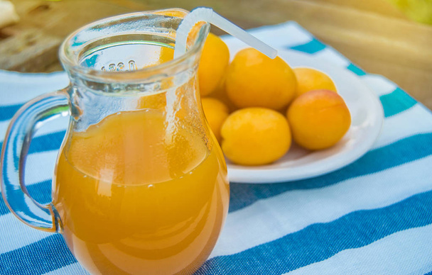 Summer drink and fruit-fresh apricot juice in a glass jug and ripe apricots on a napkin, outdoors on a Sunny day - Photo, Image