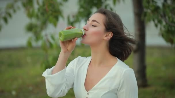 Beautiful woman drinking green smoothie outdoor - Кадры, видео