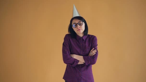 Portrait of unhappy brunette in bright party hat standing with crossed arms - Felvétel, videó