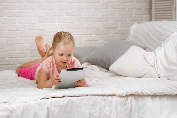 little child girl lies in bed uses digital tablet. - Fotoğraf, Görsel