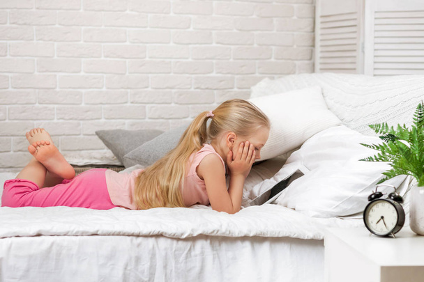 little child girl lies in bed uses digital tablet. - Фото, зображення